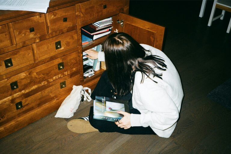 Young woman kneeling and reaching into a wooden bookshelf