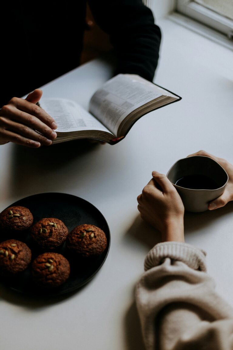 Overhead view of a person reading a book at a table with coffee and muffins