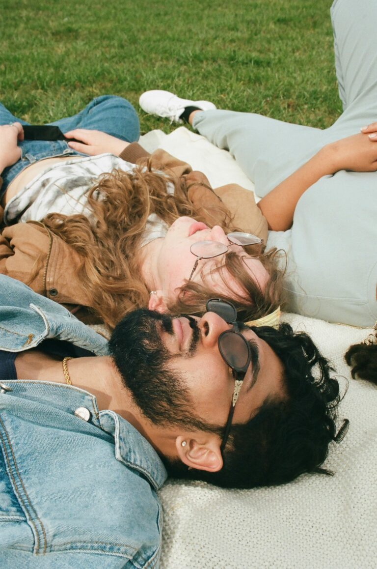 Group of young adults wearing sunglasses lying together on a blanket in the grass