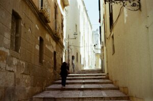 Person walking alone up stone steps in a narrow European-style alleyway
