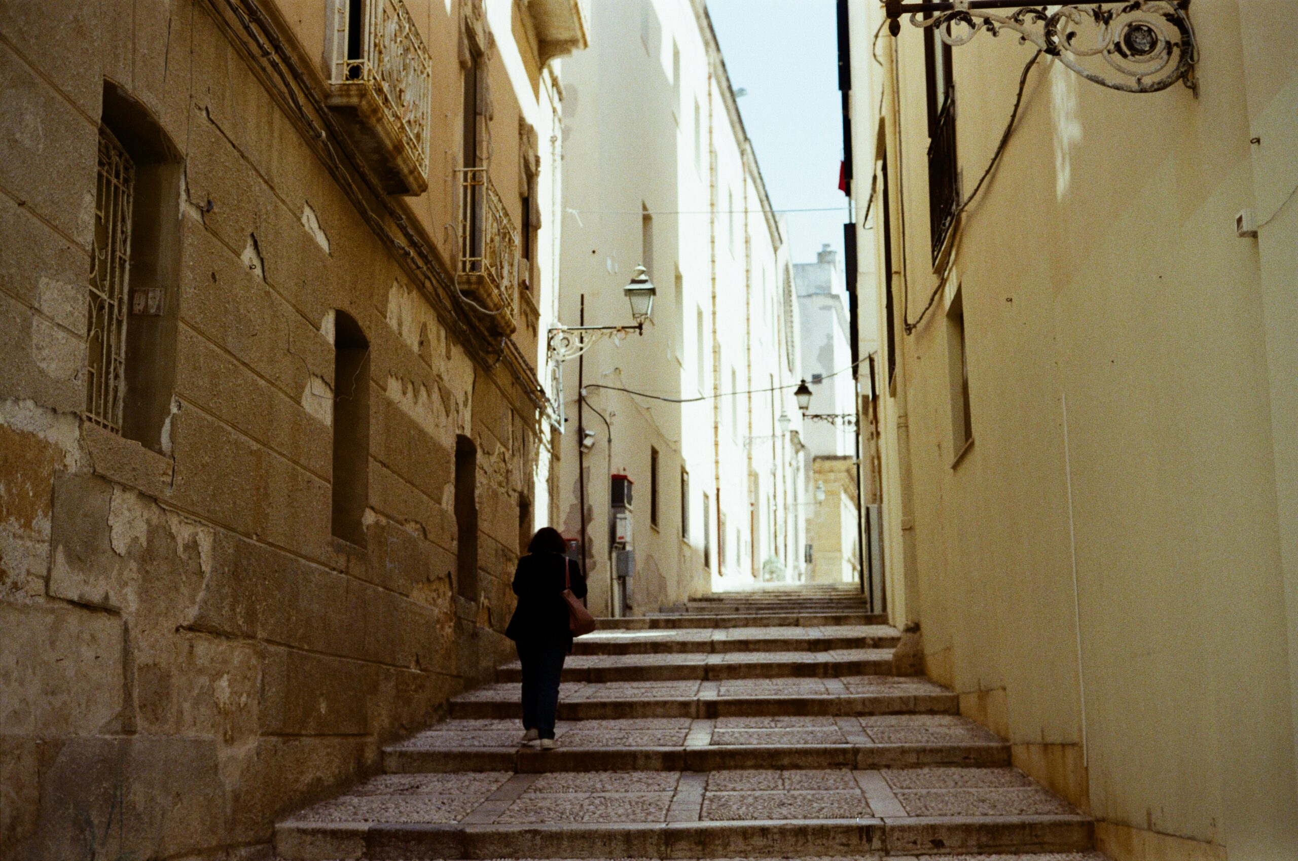 Person walking alone up stone steps in a narrow European-style alleyway