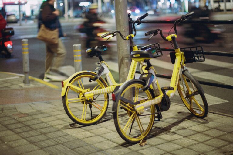Yellow shared bicycles parked on a city sidewalk at night with blurred pedestrians