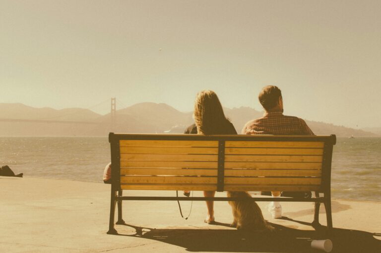 Two people sitting together on a bench at golden hour looking out at the water