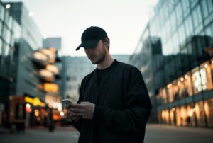 Young man in a black shirt standing on a city street at dusk with glass buildings behind him