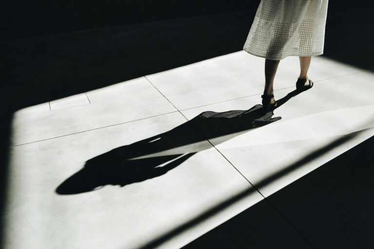 Woman walking in sunlight casting a long shadow on white pavement