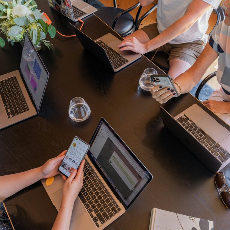 Overhead view of people scrolling on phones and laptops around a table