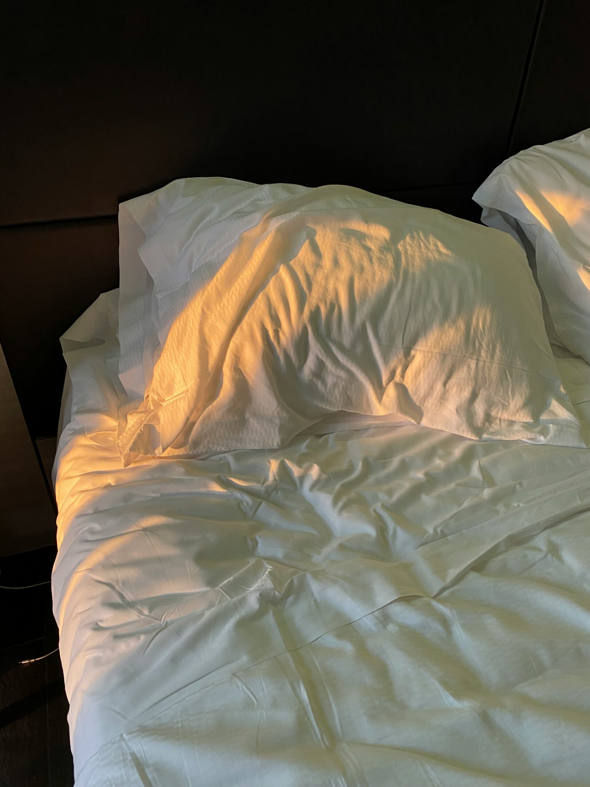 Unmade bed with white sheets illuminated by warm golden sunlight