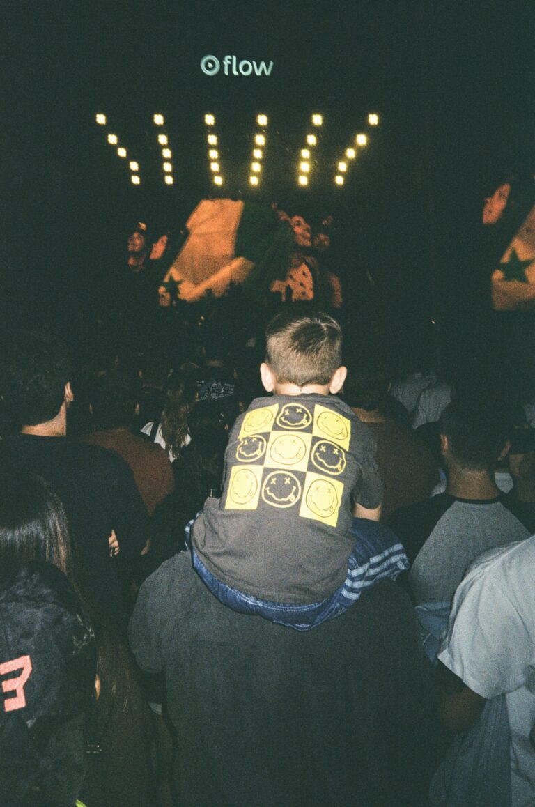 Young man sitting on someone's shoulders at a concert surrounded by a crowd
