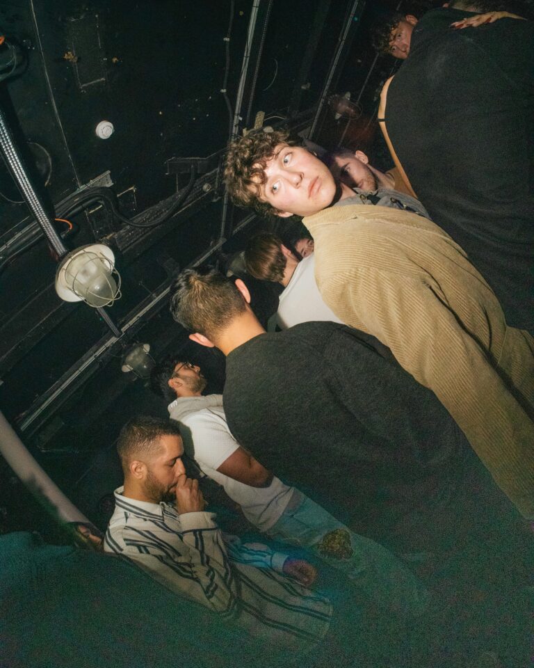 Young people crowded together in a dimly lit venue looking upward