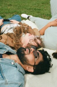 Group of young adults wearing sunglasses lying together on a blanket in the grass
