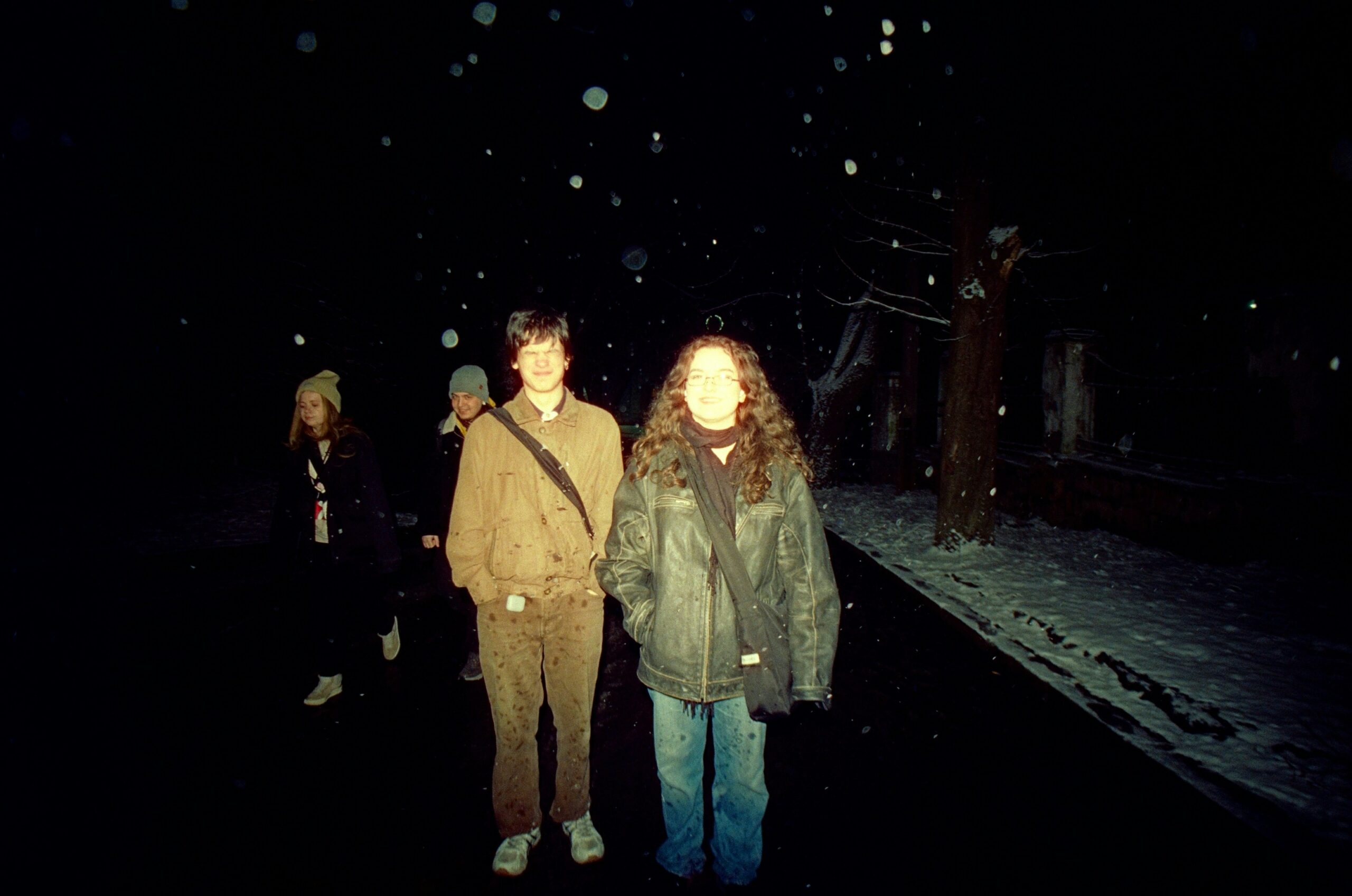 Young people walking together outside at night in falling snow captured with flash photography