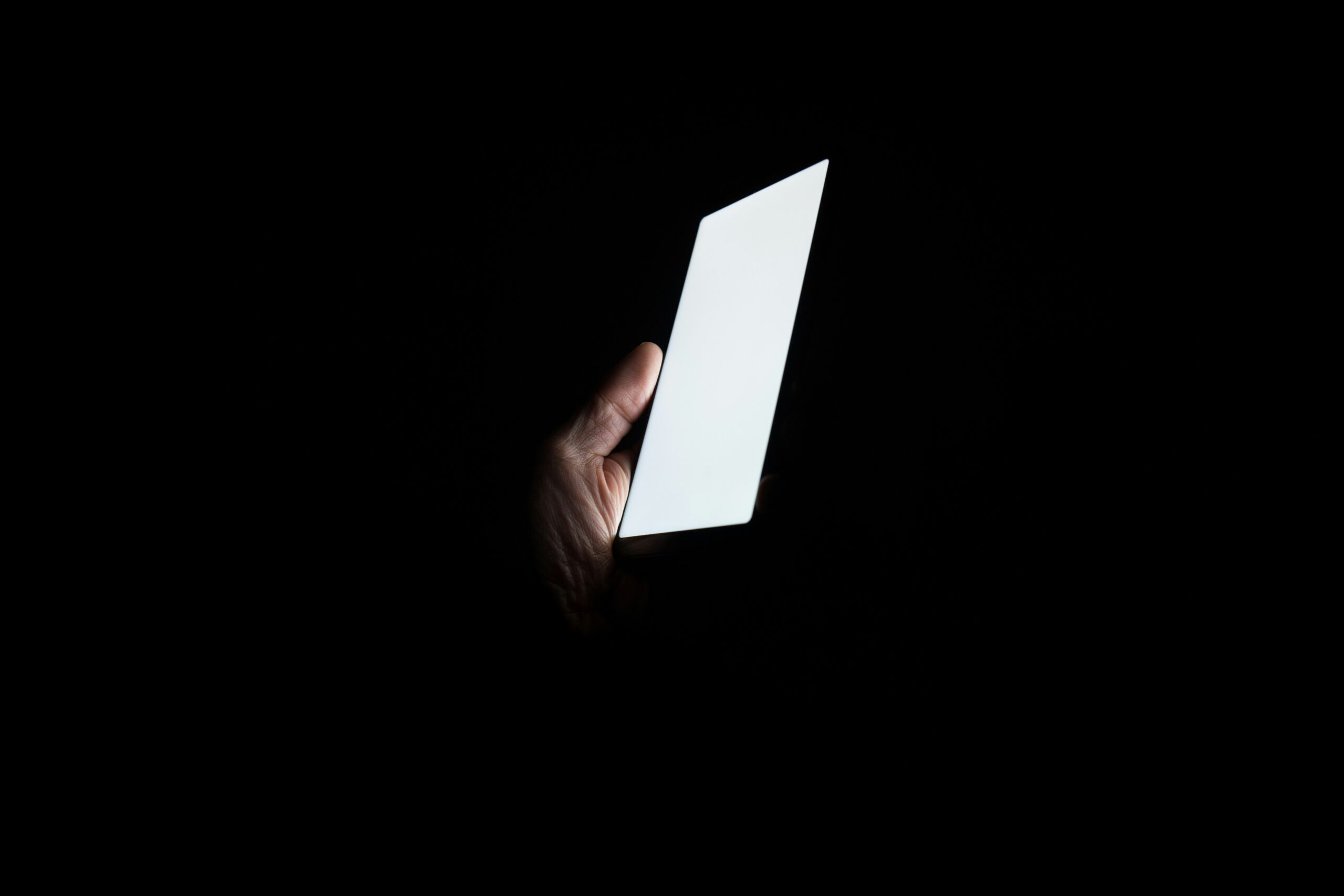 Hand holding a glowing phone screen in complete darkness