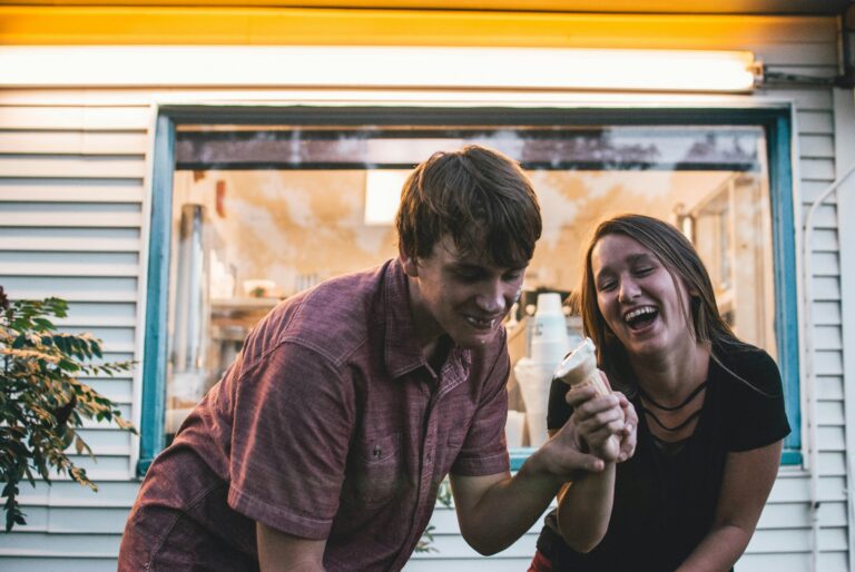 Young Christian couple laughing together while sharing an ice cream cone outside a vintage walk-up window
