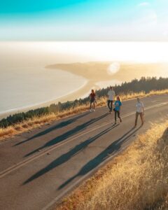 Group walking together along a coastal road at golden hour with long shadows stretching behind them