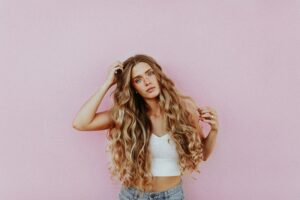 Young woman with long wavy hair in a white top standing against a pink wall, representing freedom from purity culture shame