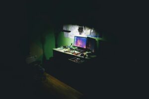 Multiple computer monitors glowing on a desk in a dark room
