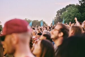 Film photo of a man in a maroon cap standing apart from a crowd at an outdoor gathering