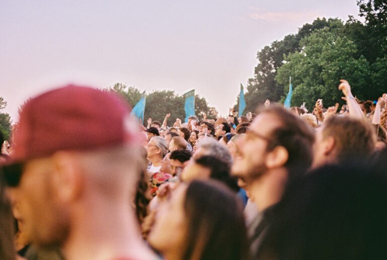 Film photo of a man in a maroon cap standing apart from a crowd at an outdoor gathering