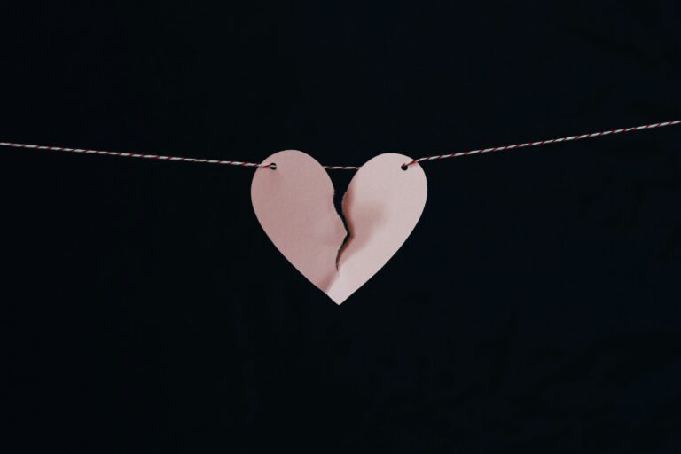 Pink paper heart torn in half hanging on a string against a black background