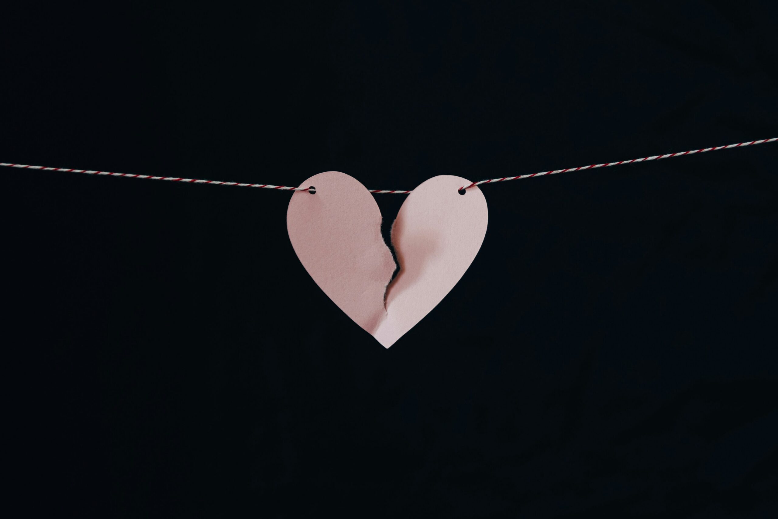 Pink paper heart torn in half hanging on a string against a black background