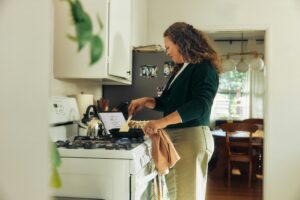 Woman cooking at a home stove with a recipe propped on a tablet beside her