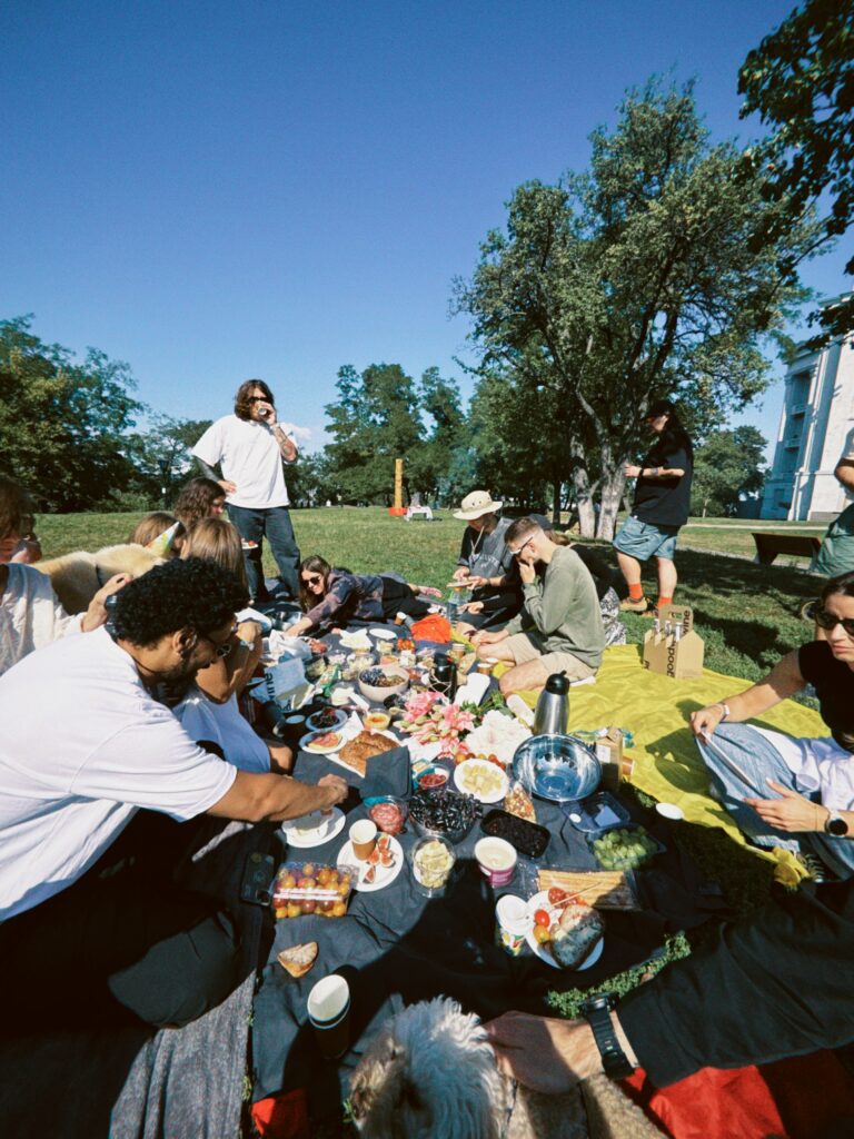 Let's Talk About It Podcast - Dating When Everyone Knows Everyone: a group of friends sharing a picnic spread on blankets under trees in a sunny park
