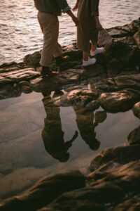Let's Talk About It Podcast - Asking Married Christian Men What Nobody Tells You About Marriage: couple walking hand in hand across a rocky shoreline at sunset, reflected in a tide pool