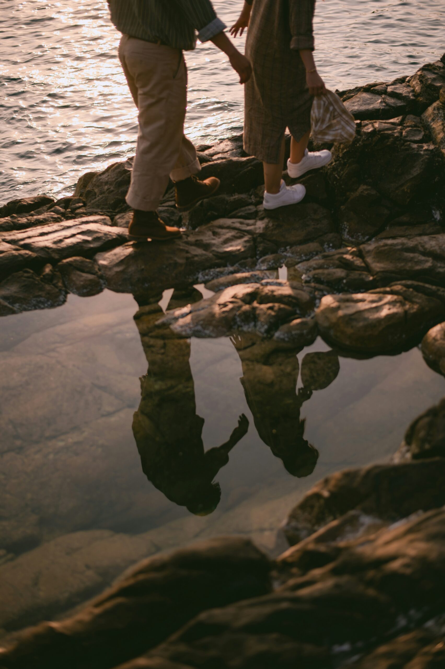 Let's Talk About It Podcast - Asking Married Christian Men What Nobody Tells You About Marriage: couple walking hand in hand across a rocky shoreline at sunset, reflected in a tide pool
