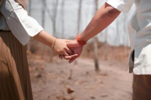 Close-up of a married couple holding hands on a dry dirt path, his white shirt and her white blouse and brown skirt, a grip that holds when marriage brings out the worst in you