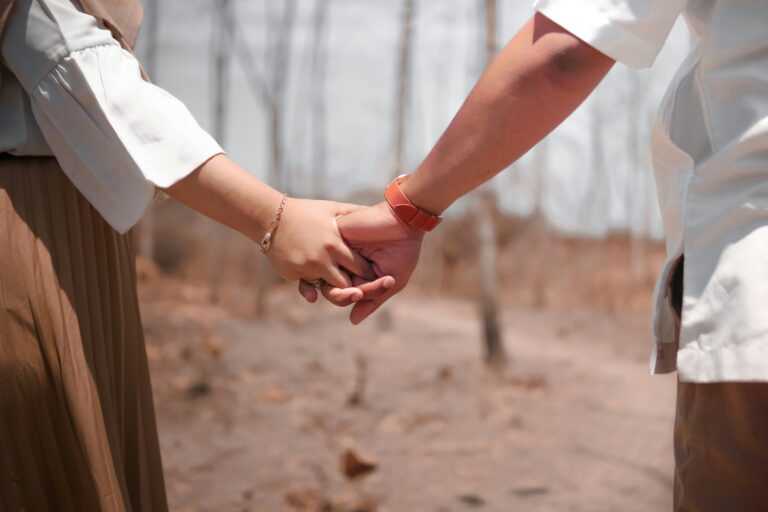 Close-up of a married couple holding hands on a dry dirt path, his white shirt and her white blouse and brown skirt, a grip that holds when marriage brings out the worst in you
