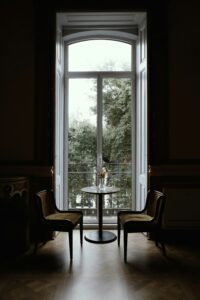 Two chairs and a small round table beside a tall window overlooking trees.